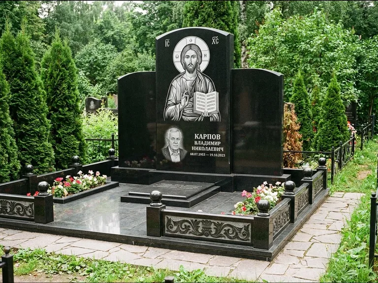 Памятник с гравировкой иконы: широкая панорамная стела с золочёным нимбом — гравировка образа Матроны Московской, цветник с белыми хризантемами, работа «Мельникова» в Воронеже